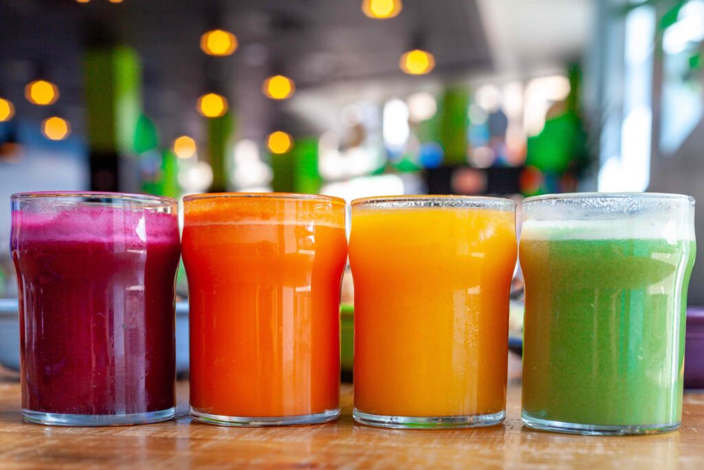 Four glasses of juice in purple, orange, yellow, and green sit on a counter top in Square Cafe.