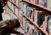 Summer Reading Recommendations from Pittsburgh Booksellers A brunette girl examines books at a bookstore, drink in hand