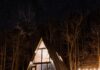 Weekend Getaways Close to Pittsburgh A photo of a triangle weekend getaway house in the middle of the woods, lit up from the inside at night.