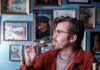 Where to Taste Wine in Pittsburgh Adam Knoezer leans against a bar in Pittsburgh as he sips from a wine glass while surrounded by various wine bottles.