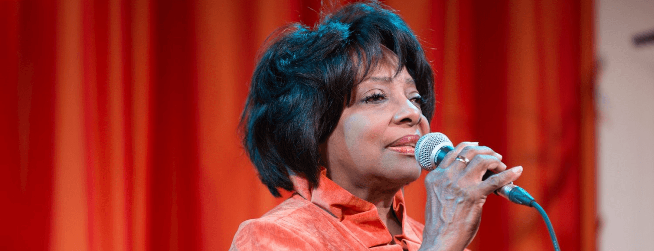 Etta Cox sings into a microphone in an orange jacket in Pittsburgh.