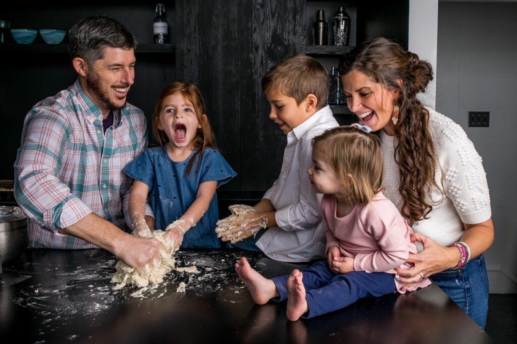 Dad, two daughters, son, and mom knead a pizza dough on a black table.