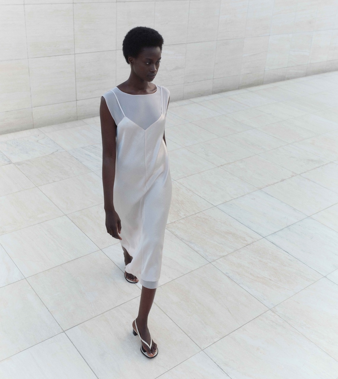 A woman in a white dress from a local Pittsburgh shop walks across white tiles.