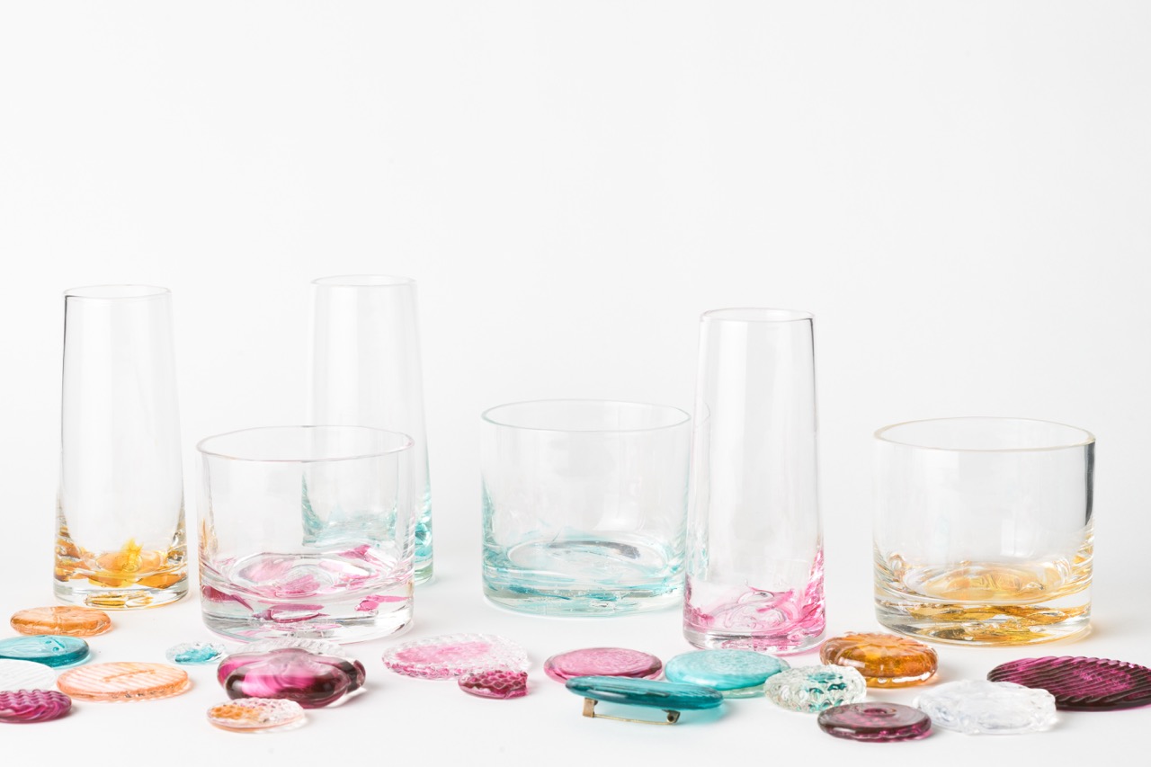 Clear glasses with pink, blue, yellow, and purple tints at the bottom sit on a white backdrop.