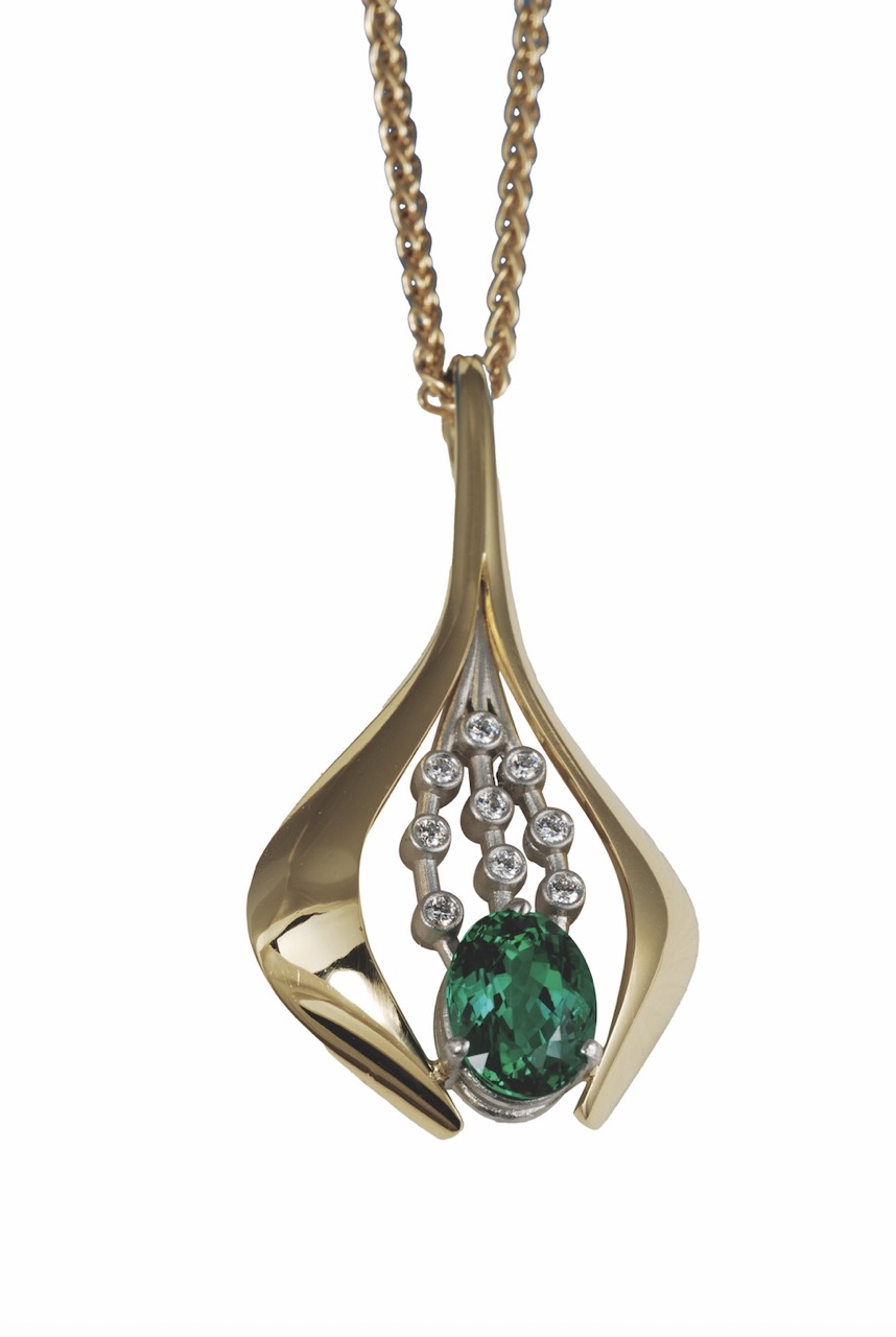 A brass necklace in a unique shape with a green jewel in the center sits against a white background.