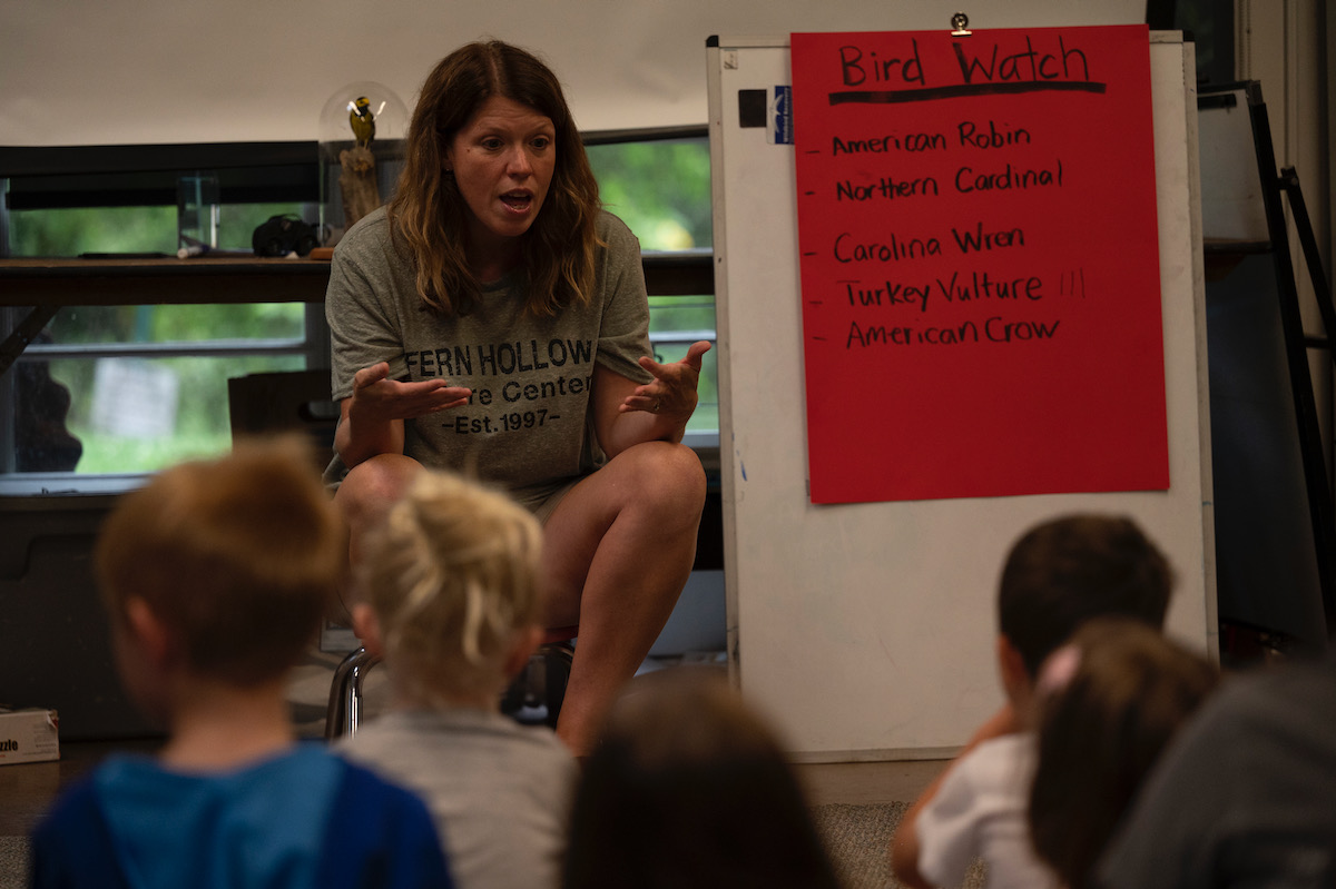 A woman speaks to a group of children about bird-watching, next to a red paper sign about it 