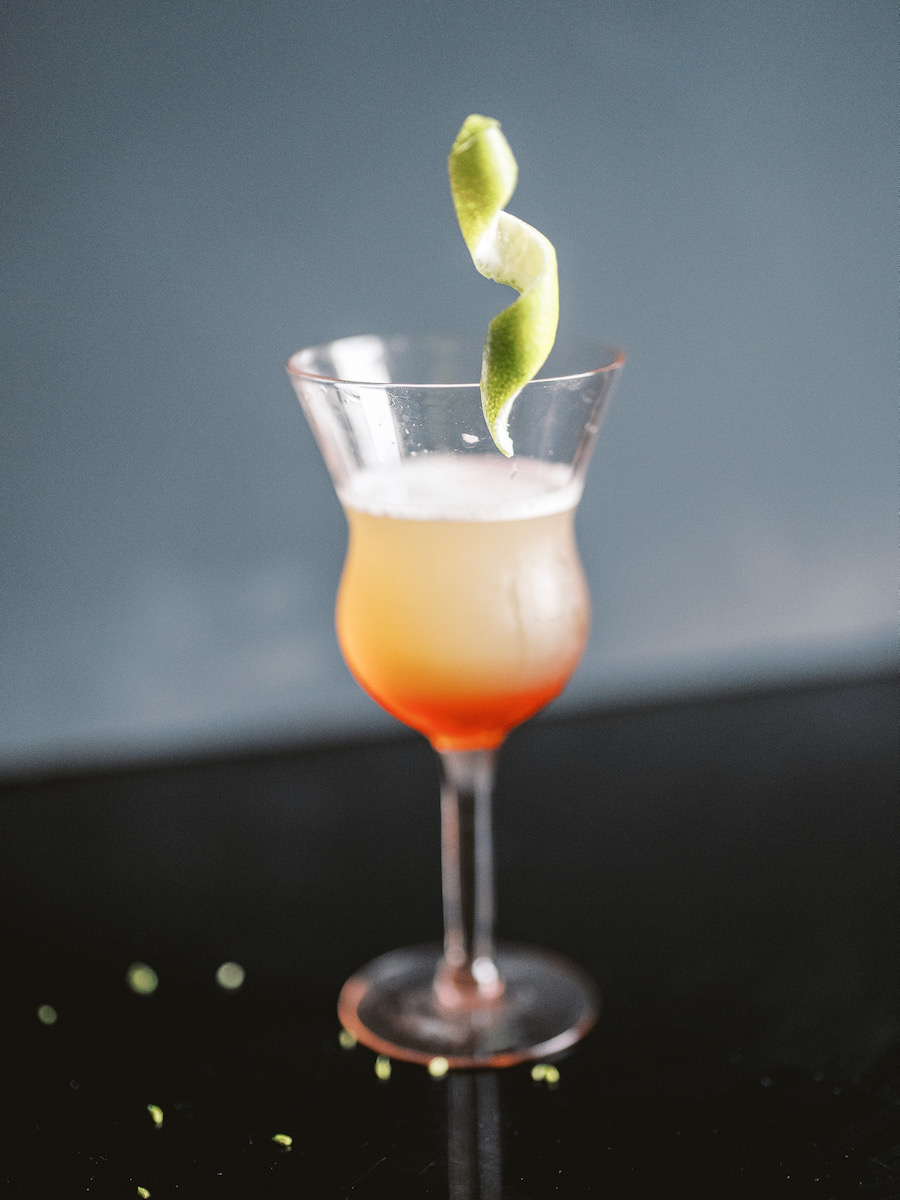 A yellow and red gradient Jungle Bird cocktail on a black background