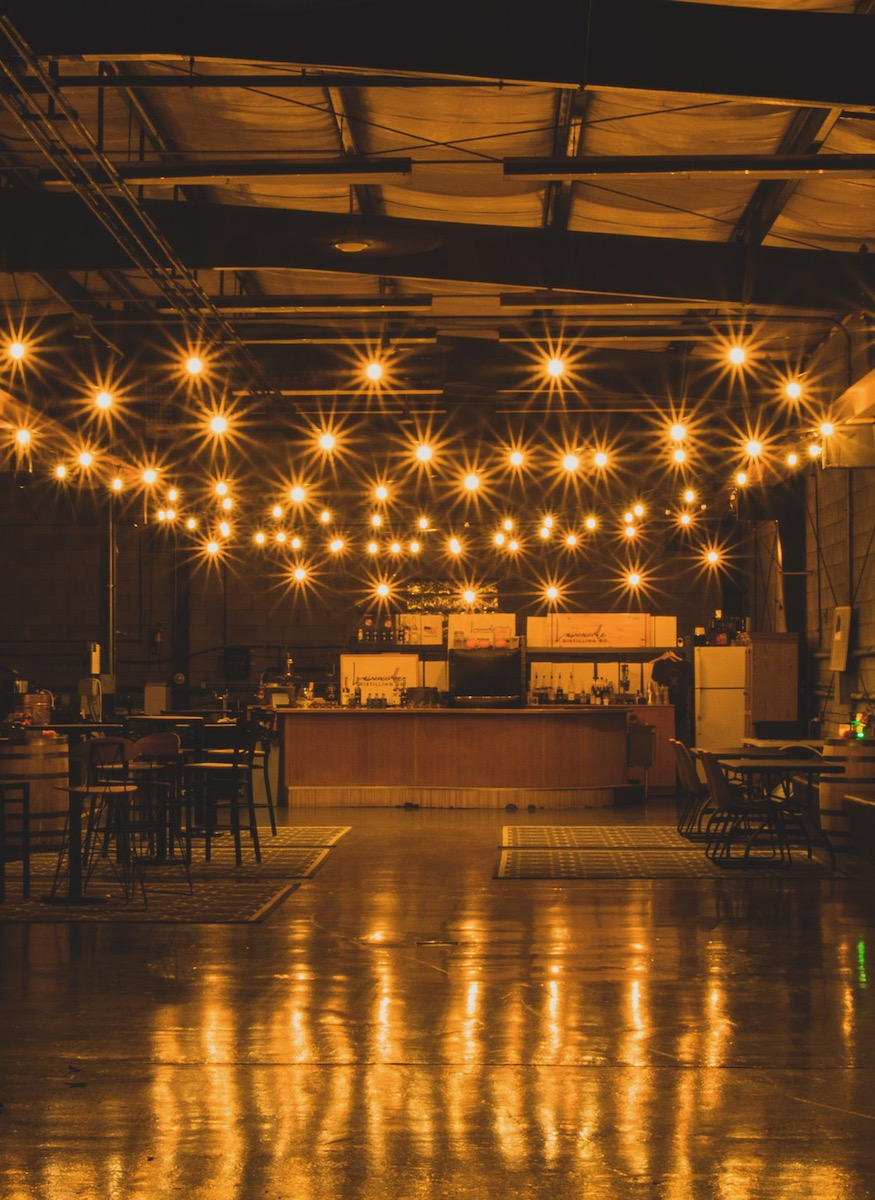 A dimly lit tasting room with a bar and stills in it