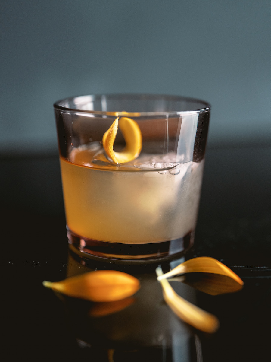 A mezcal cocktail with orange peel on a black background