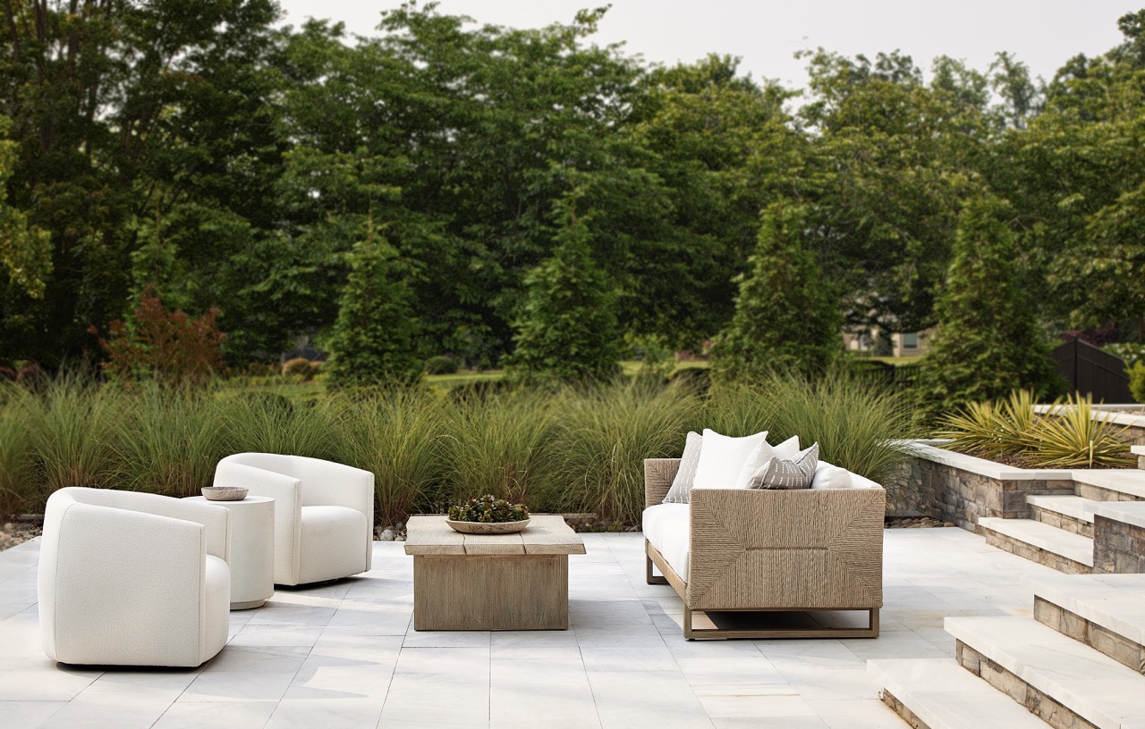 White outdoor chairs and a white outdoor couch sit on a deck with a brown and white table between them.