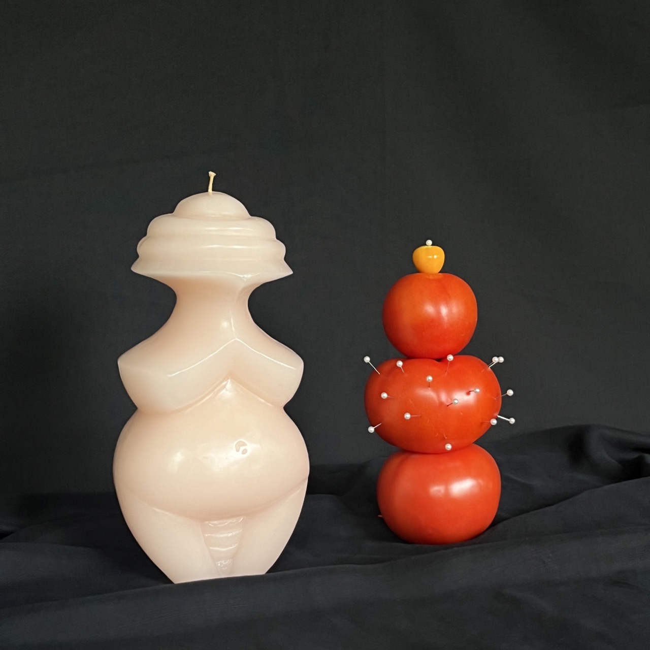 Two bulbous candles one in white and one in red sit beside each other on a black background.