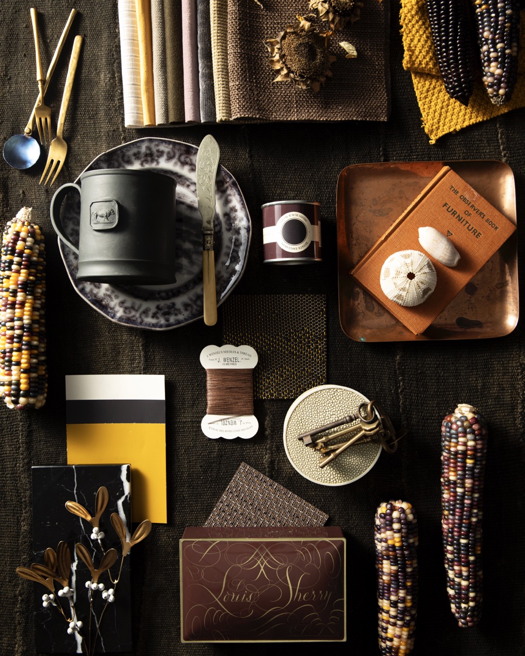 Various indigenous design objects sit on a black backdrop such as a spool of threat, Indian corn, and utensils. 