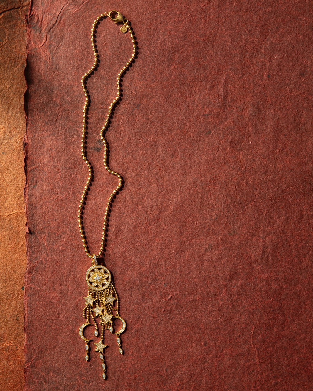 A native dream catcher necklace in gold yellow sits against a red sheet of paper. 