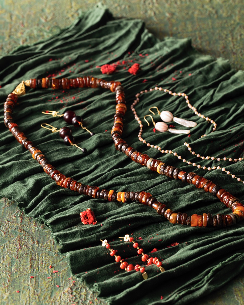 Various red necklaces and earrings sit on a green fabric.