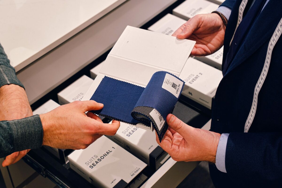 Fabric swatches in shades of blue and grey held by a man's hands with another man touching them.