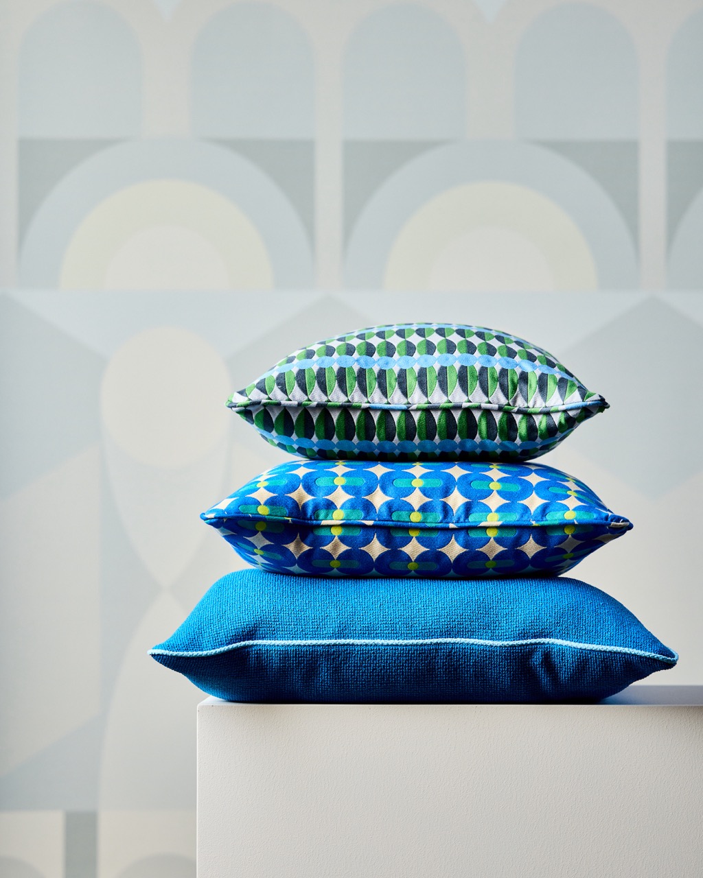 A stack of blue solid and patterned pillows sits on a white stand.