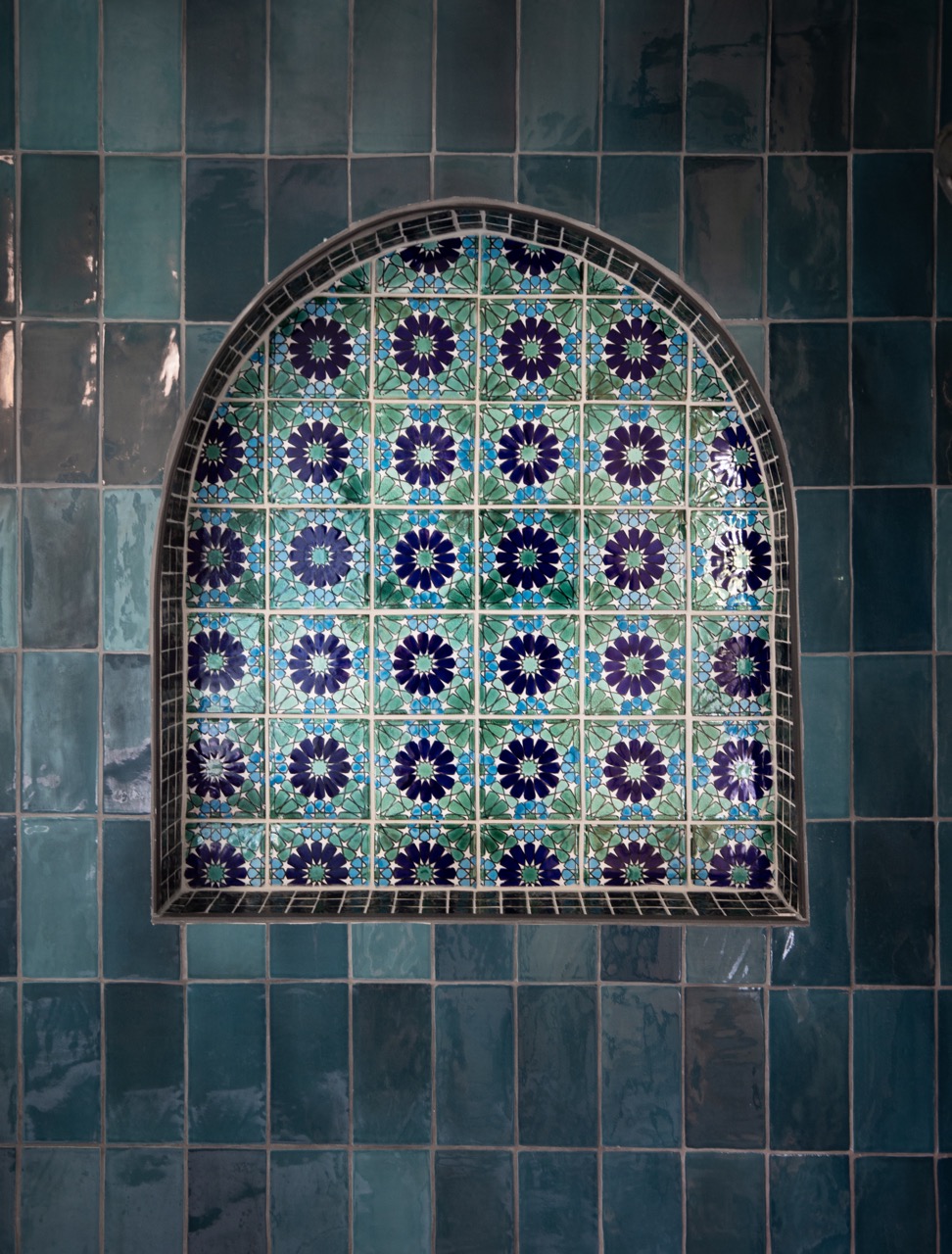 A blue and grey tile wall with an arching patterned tile in the center.