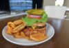 Football Season Arrives at Rivers Casino Pittsburgh A cheeseburger on a white plate with lettuce, tomato, onion, and pickle stacked on the top, surrounded by waffle and thick cut French fries at Rivers Casino Pittsburgh.