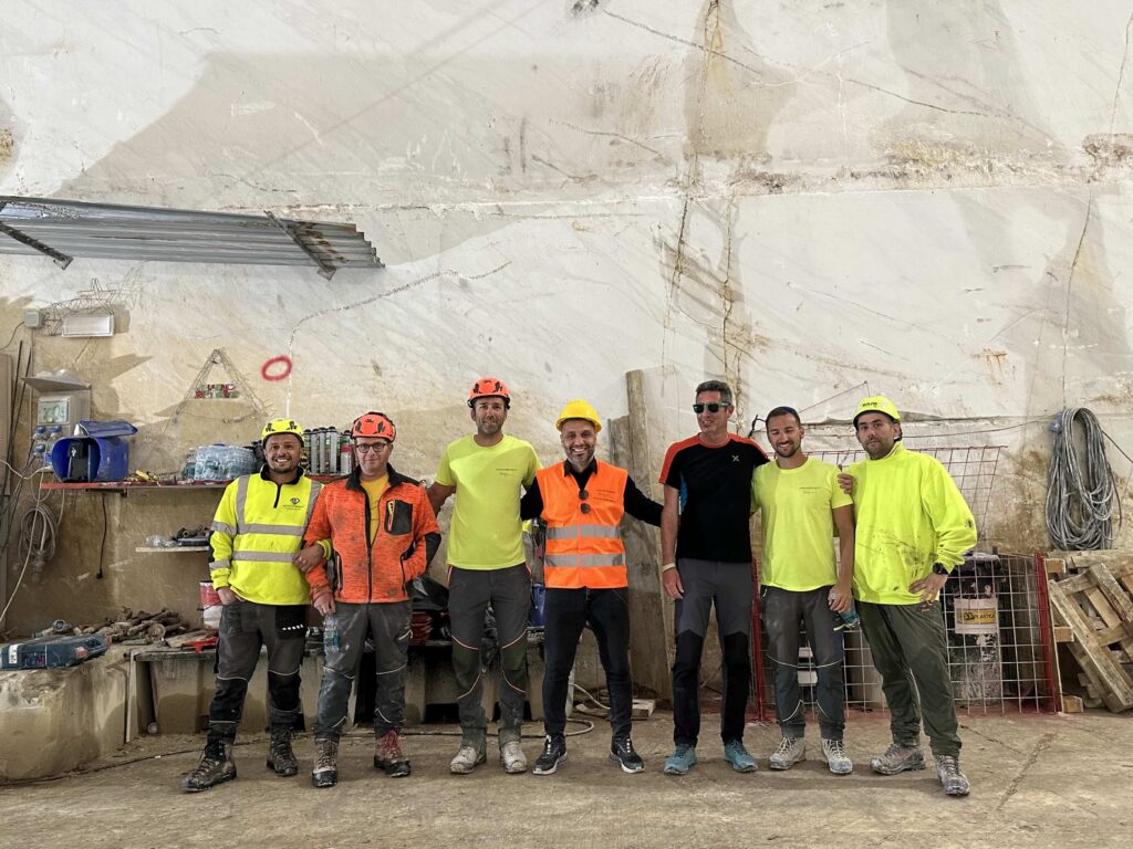 A group of men construction workers in neon gear stand in front of a quarry marble wall.