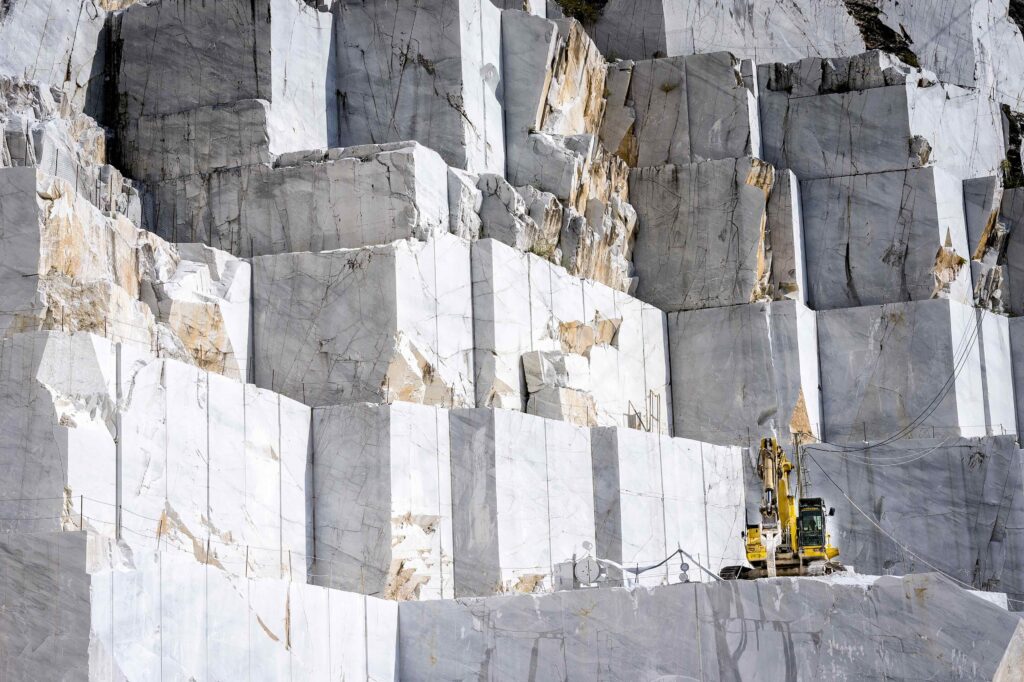 A series of cube shaped marble quarry blocks in Carrara, Italy with a yellow construction vehicle sitting on one of the blocks.