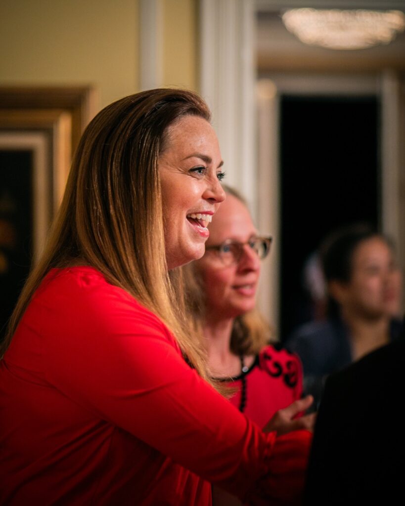 A woman in red smiles and shakes hands with another Halloween party guest.