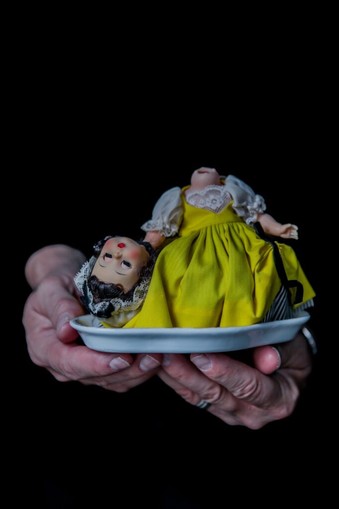 A baby doll sits on a plate with its head cut off beside it.