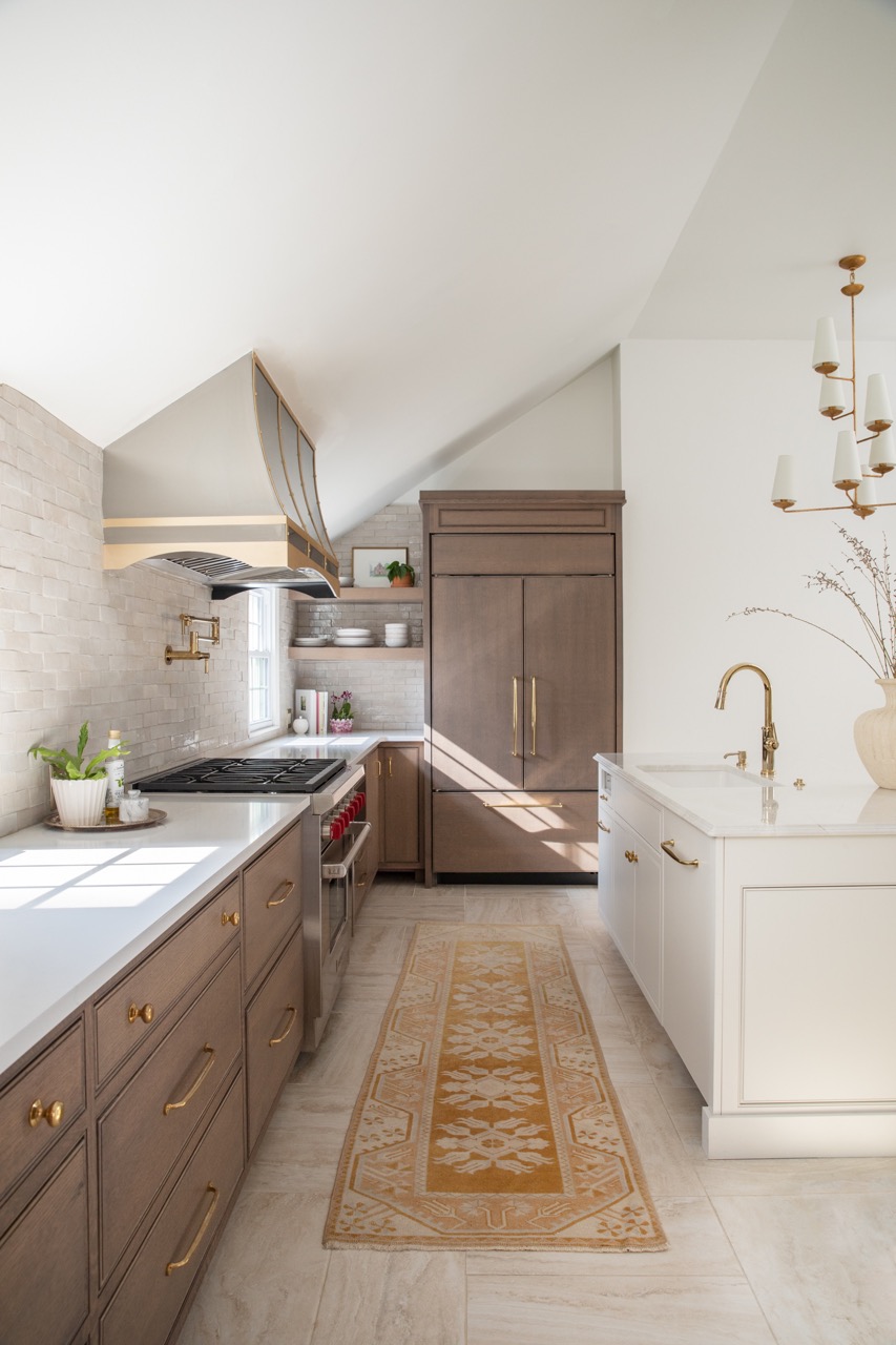 A longshot of a kitchen with a white sink with a gold faucet to the right, a wood cabinet with a white marble countertop, and a wood cabinet in the background.