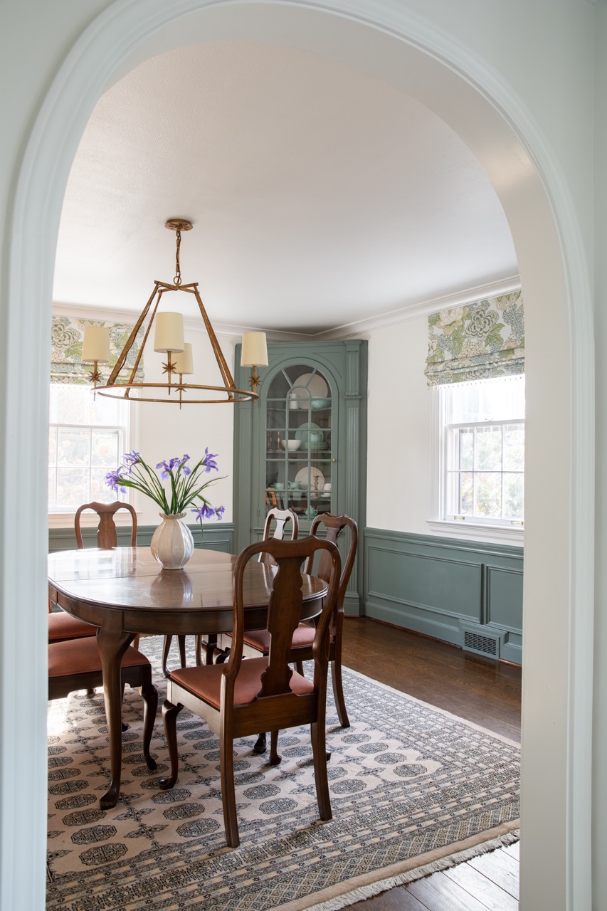 Through an archway sits a brown dining table with chairs around it and then blue embellishments against the white walls. 