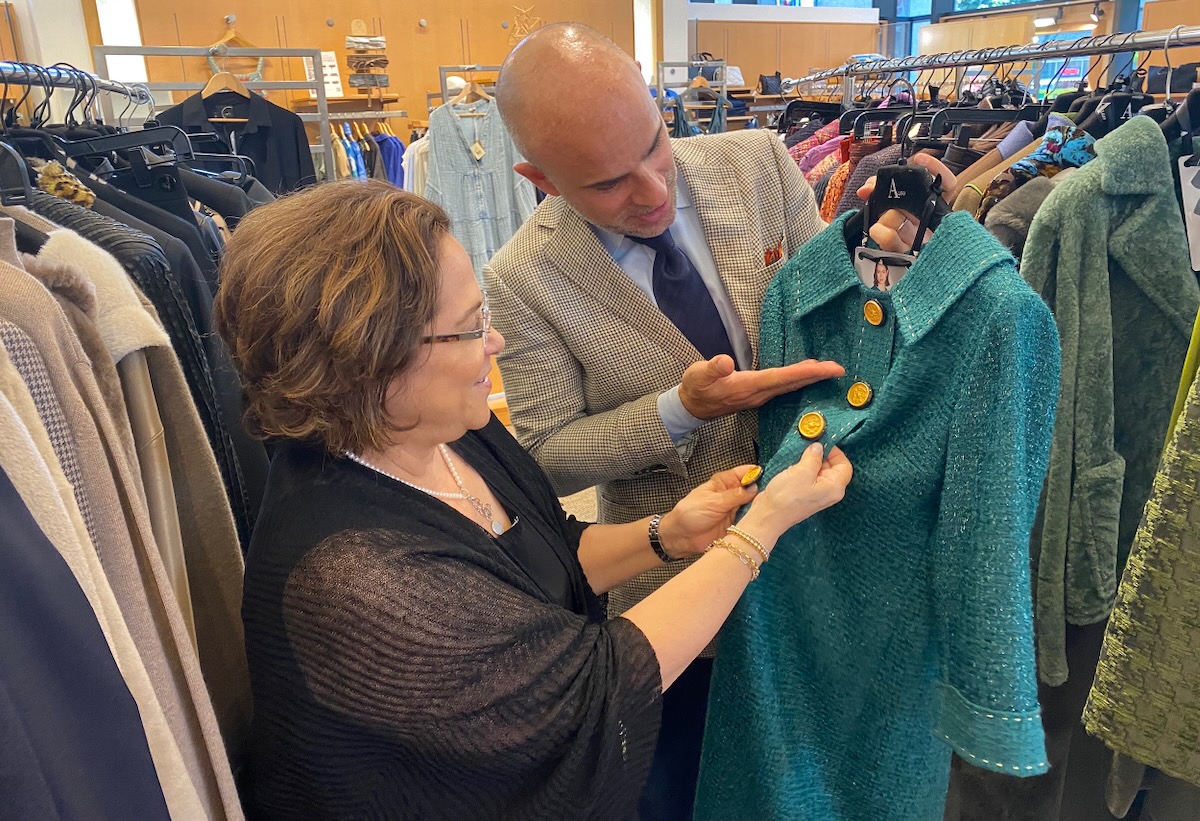 A man and a woman looking at the buttons on a women's teal coat. 