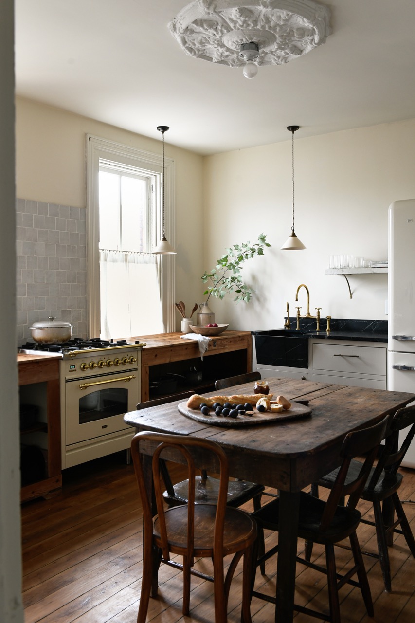 A kitchen with a dark wood table in the middle and counters on the wall but white/beige walls behind them.