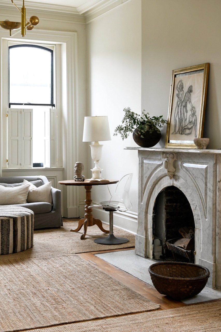 The interior of a renovated townhouse living space with white walls, a white fireplace, and a white lamp.