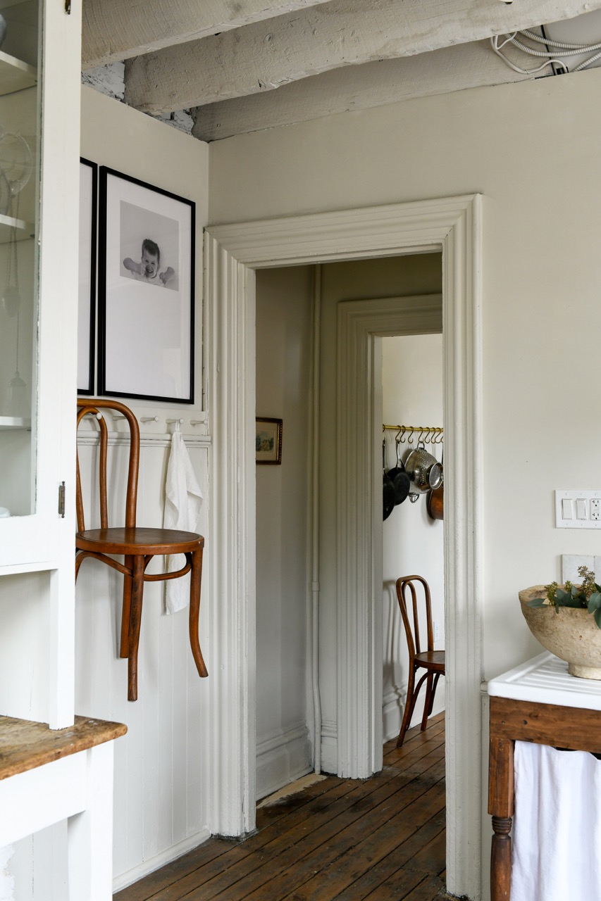 The entrance between two rooms featuring white walls, cabinets, and a brown chair hanging on the left wall.