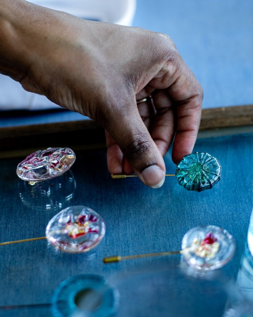 A woman's hand picks up a small round textile attached to a small metal stick.