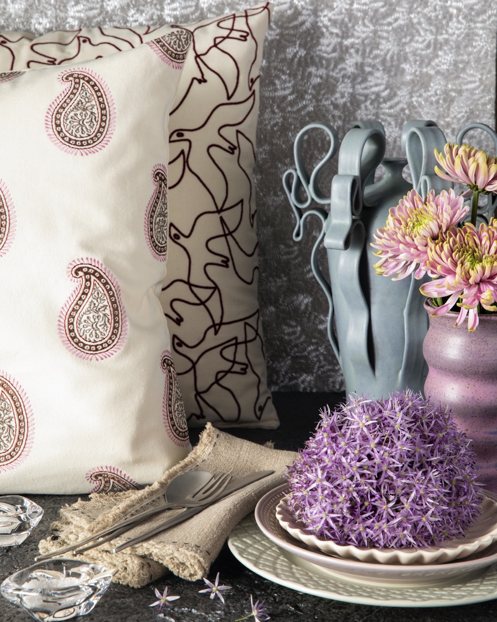 A paisley nostalgia pillow sits beside two funky, bright colored vases.