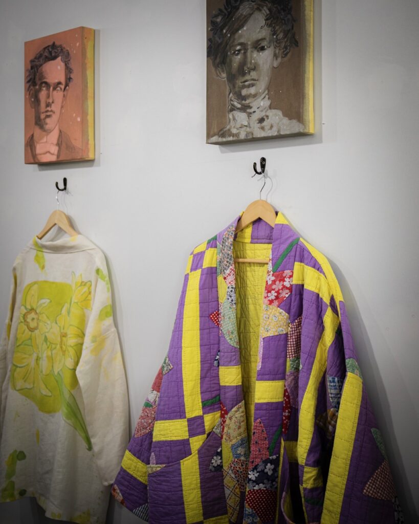 Two custom color blocked jackets hang on a wall below two old pictures.