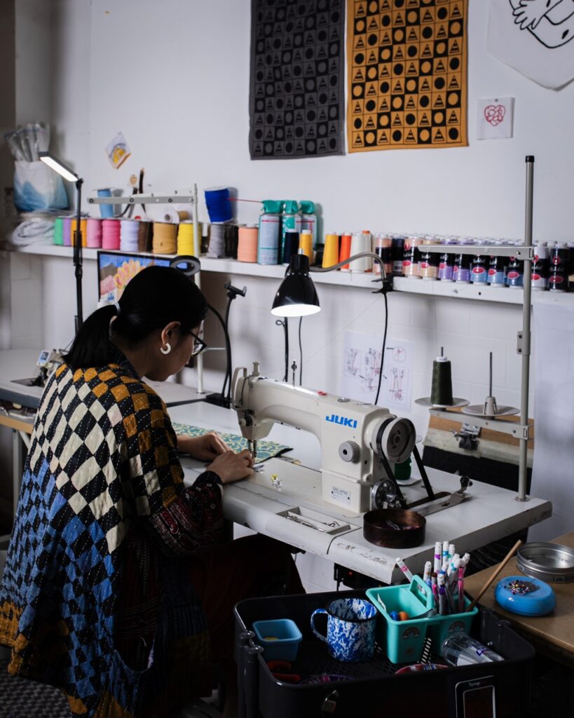 Rona Chang sits in a chair, sewing at her work station.