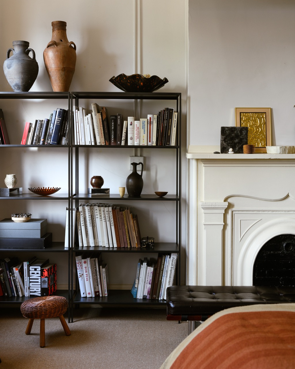 A bookshelf filled with books sits against a white fireplace with vintage frames on top. 