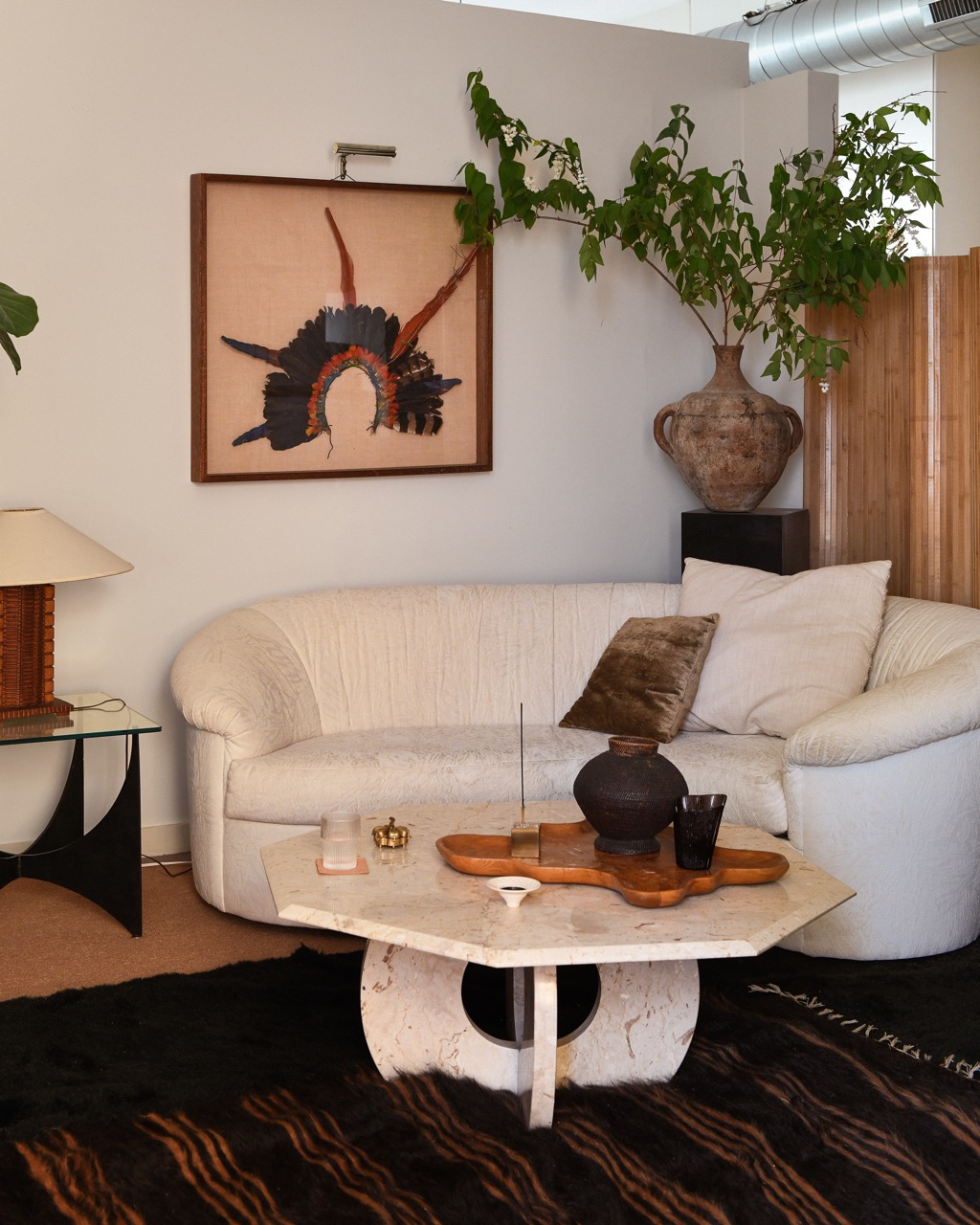 A white couch sits in the middle of a living room decorated with vintage vasus and paintings. 