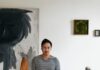 Video Game Artist Ryan Yee Hunts Down Vintage Furniture Ryan Yee stands in front of a painting, vintage furniture dresser, and podium with two statues on it.