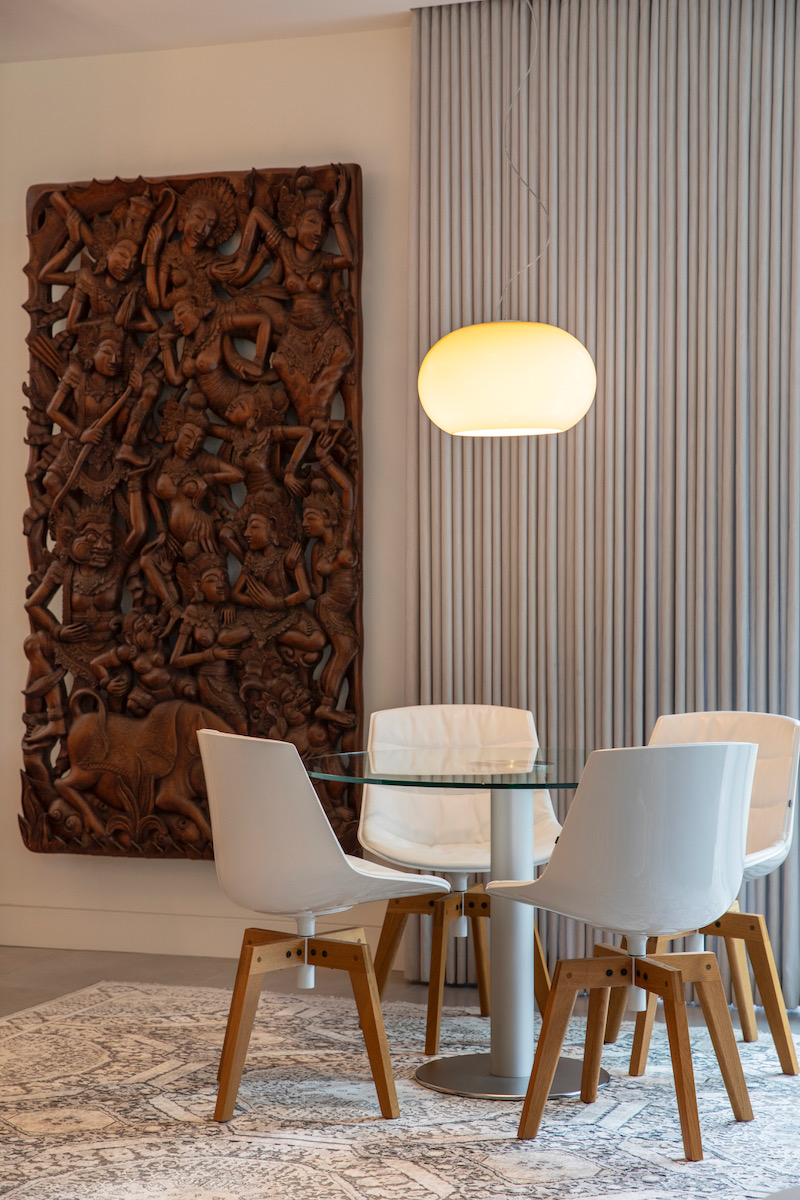 A living room with a round hanging lamp and a large woodcut piece on the wall 