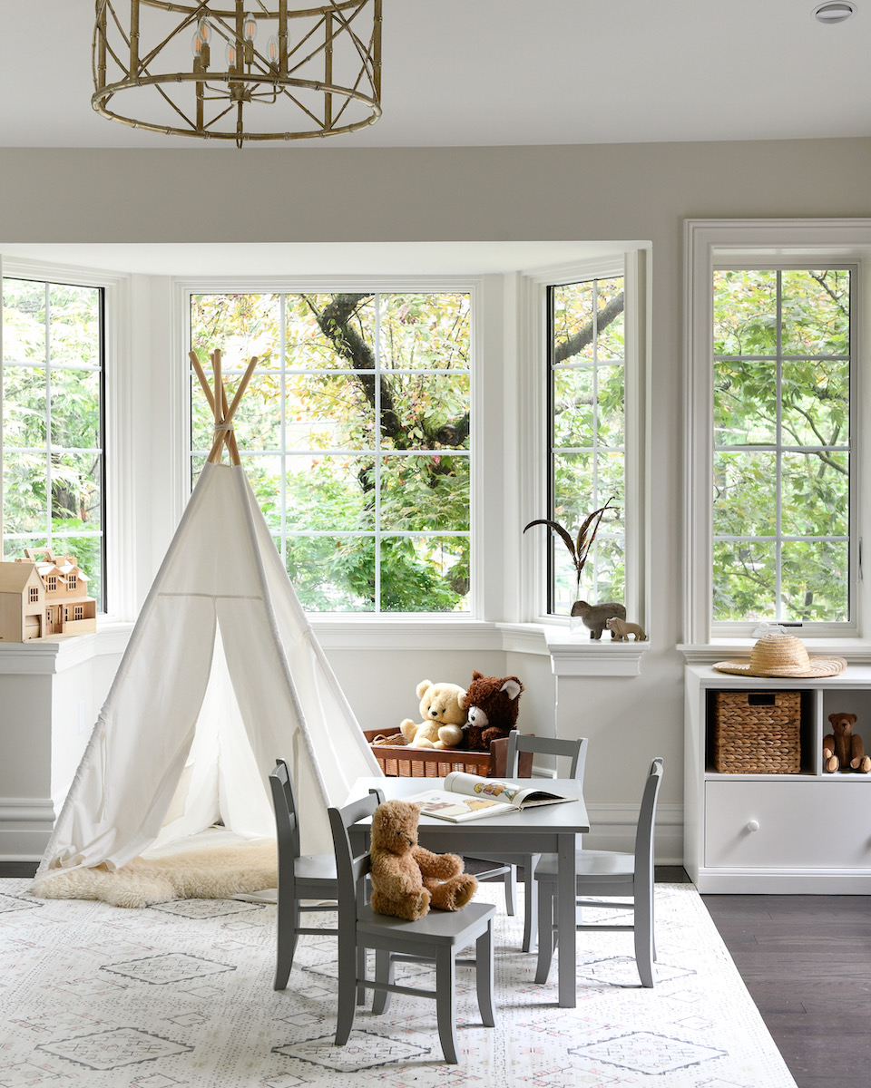 An interior with a teepee and windows, designed for kids with toys strewn across