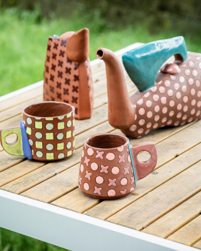 Taylor Mezo Brings a Pop of Color with Her Ceramics Various ceramics with dots all over them by Taylor Mezzo sit on a wooden picnic table.