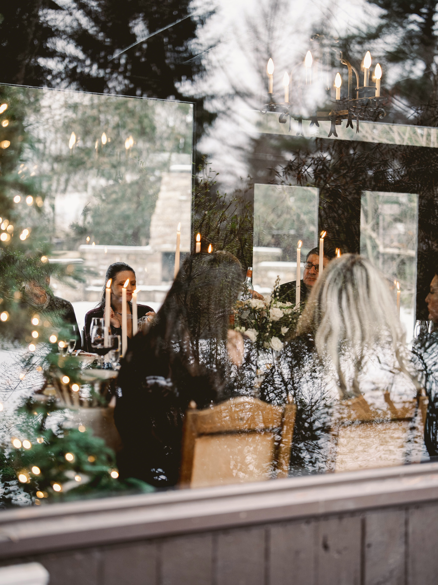 A cozy indoor dining scene showing guests enjoying a festive feast of seafood dishes by candlelight with a picturesque snowy view outside the window.