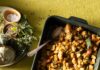 The Best Vegan Stuffing A small rectangular pan of vegan stuffing with a spoon in it sits on a green holiday table.