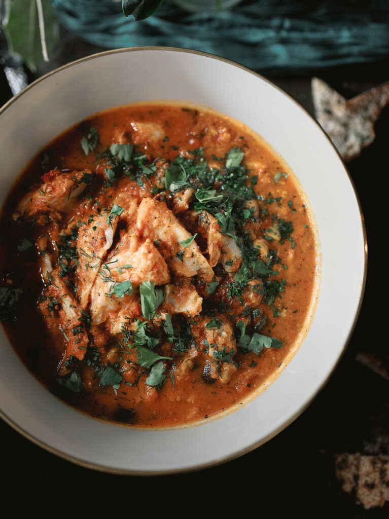 A white bowl filled with a rich tomato-based seafood Brodetto di Pesce stew topped with chopped parsley.