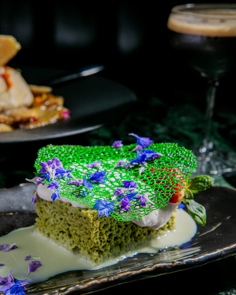 A close-up photograph of a green cake with white frosting and small blue flowers on top.