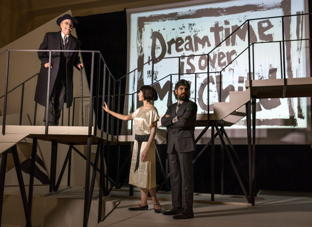 Three figures stand in front of a sign that reads "Dreamtime Is Over"