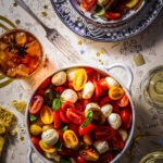 Bowl of caprese salad consisting of halved cherry tomatoes, marinated mozzarella balls and fresh basil leaves artfully arranged on a decorative white dish.