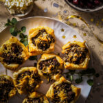 Plate of baked empanadas filled with beef, onion, and cheese mixture topped with feta cheese and served with olives.