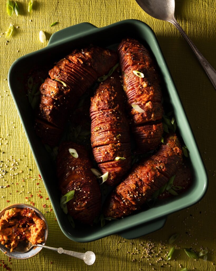 A rectangular green pan full of sliced sweet potatoes in a gochujang glaze.